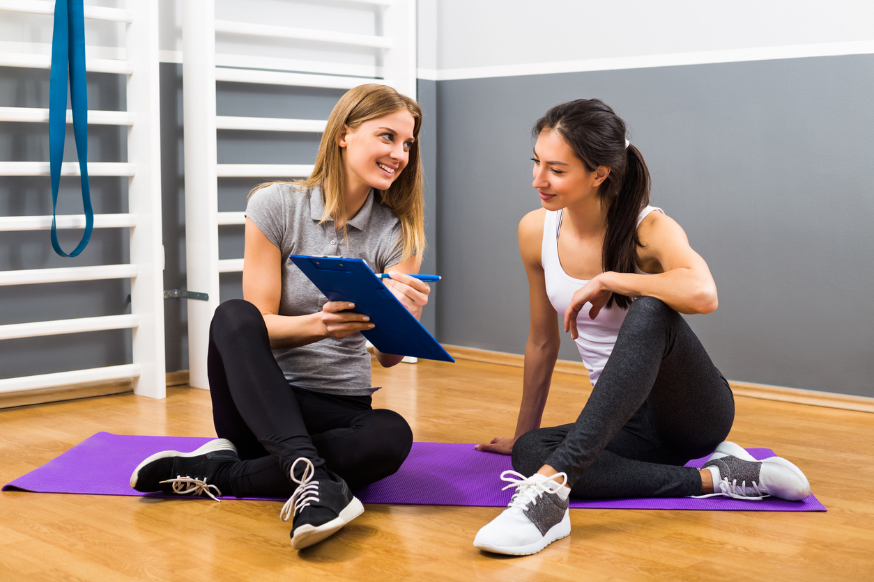 Young woman and her fitness instructor are having conversation at the gym about exercising.