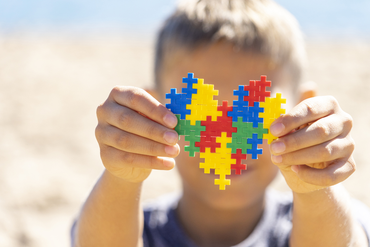 Boy hands holding colorful puzzle heart in front of his face. World autism awareness day concept.