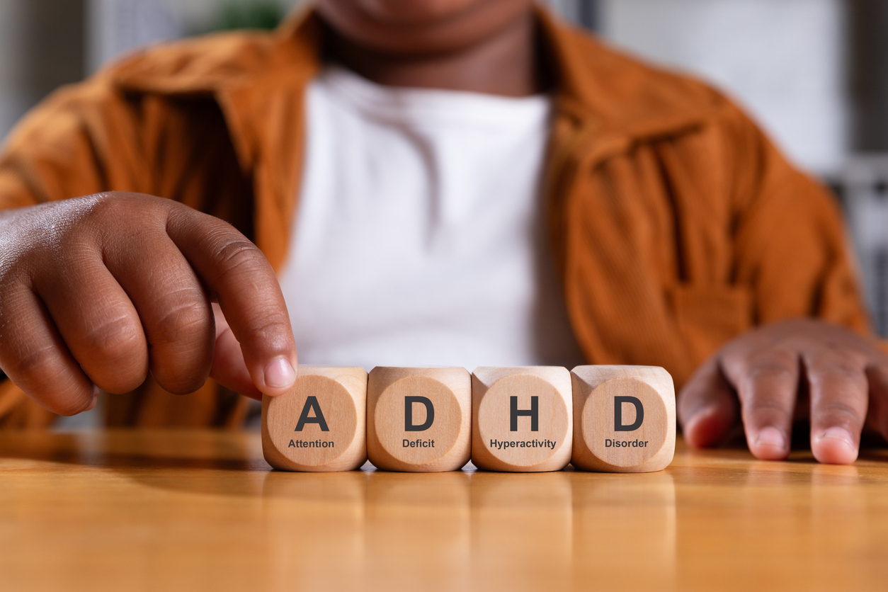 Hand of black boy puts wooden cube with ADHD, Attention Deficit Hyperactivity Disorder on table.